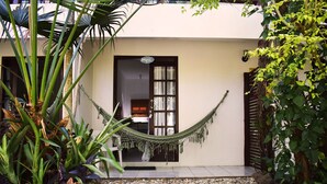 Une maison avec un hamac devant la porte, entourée de plantes et de petits cailloux.
