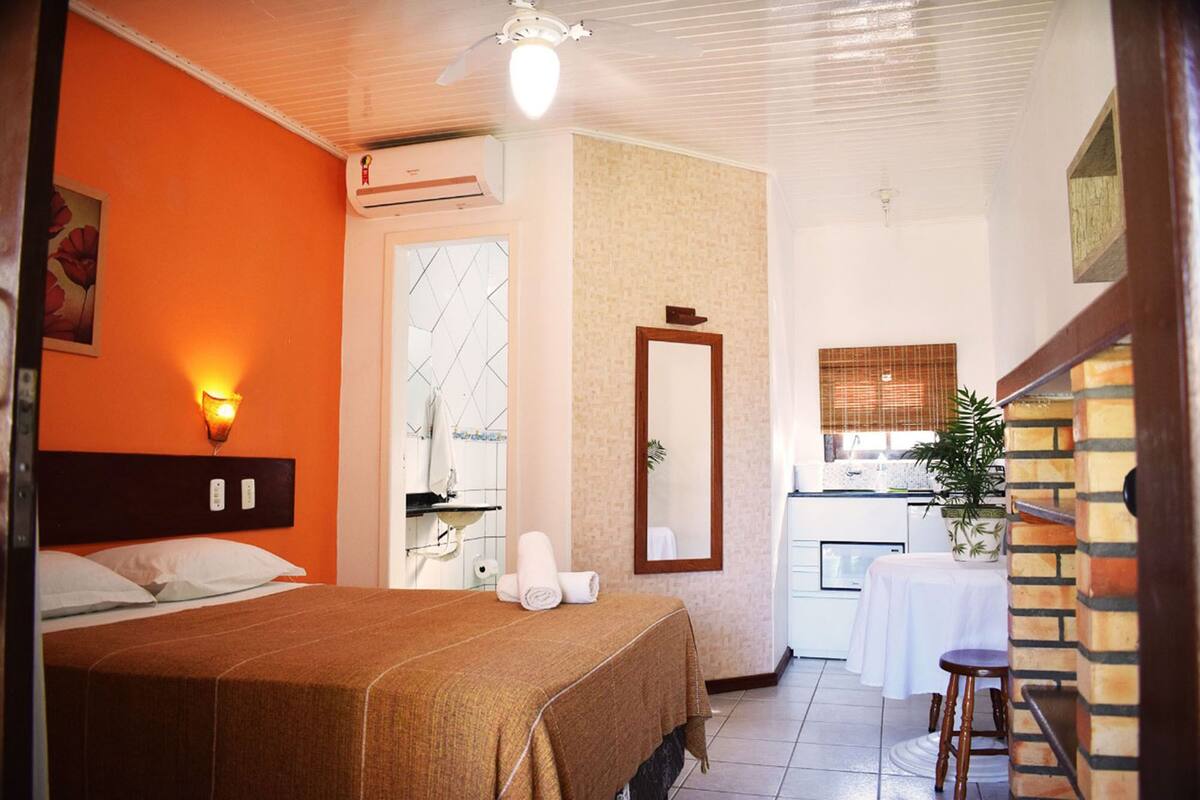 Ein Hotelzimmer mit Bett, Badezimmer mit Spiegel, einer kleinen Küchenzeile und einer Topfpflanze.