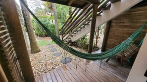 Une terrasse en bois avec un hamac, un escalier et un espace jardin agrémenté de galets et de plantes.