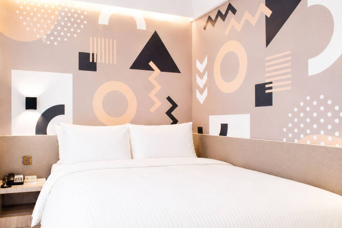 A modern hotel room with a large bed, a bedside table, and a wall with abstract geometric patterns.