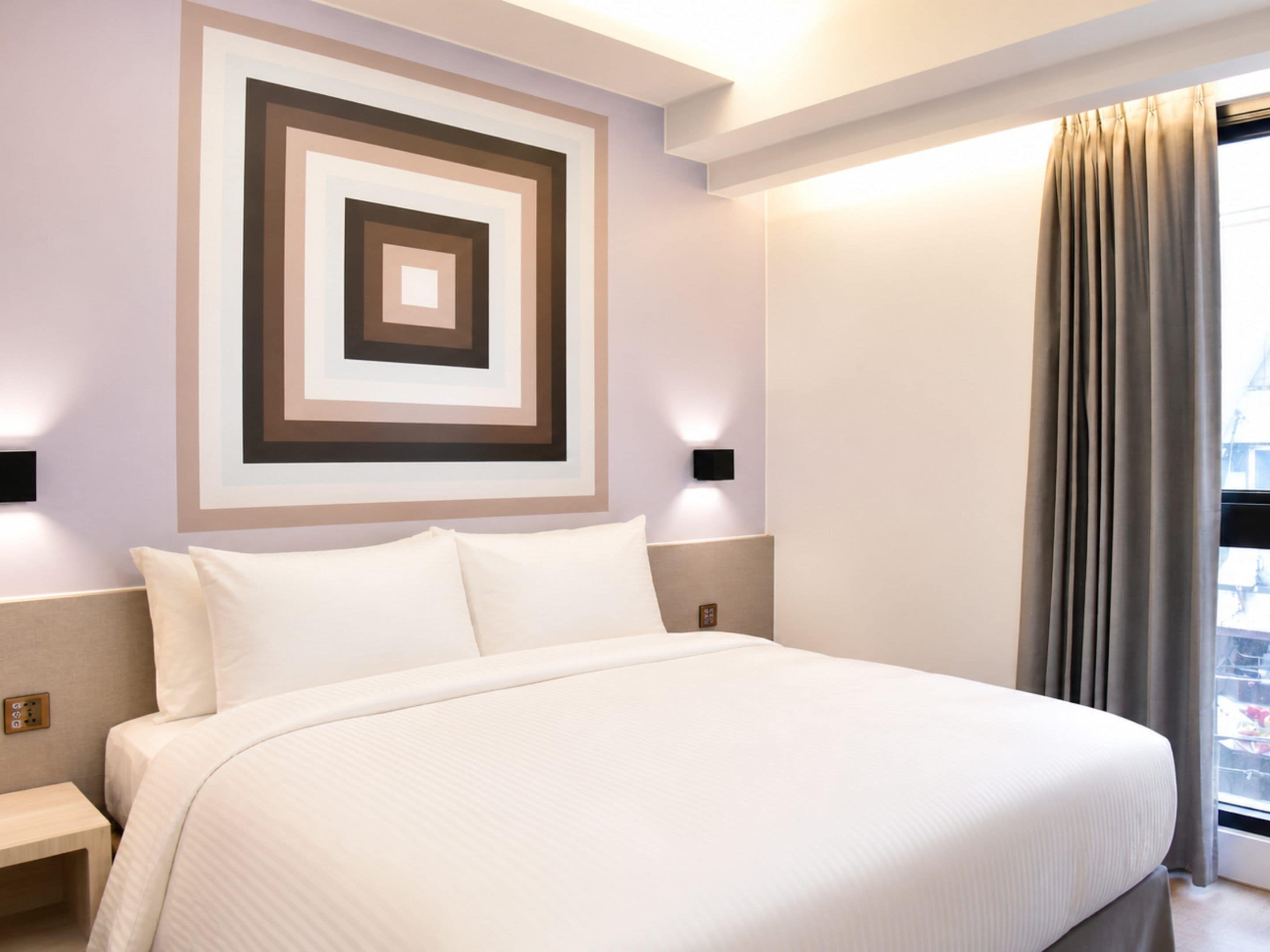 Une chambre d’hôtel avec un grand lit, une œuvre d’art murale, une table de chevet et une fenêtre avec des rideaux.