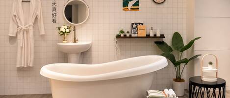A bathroom with a freestanding bathtub, a round mirror, a sink, and a shelf with toiletries.