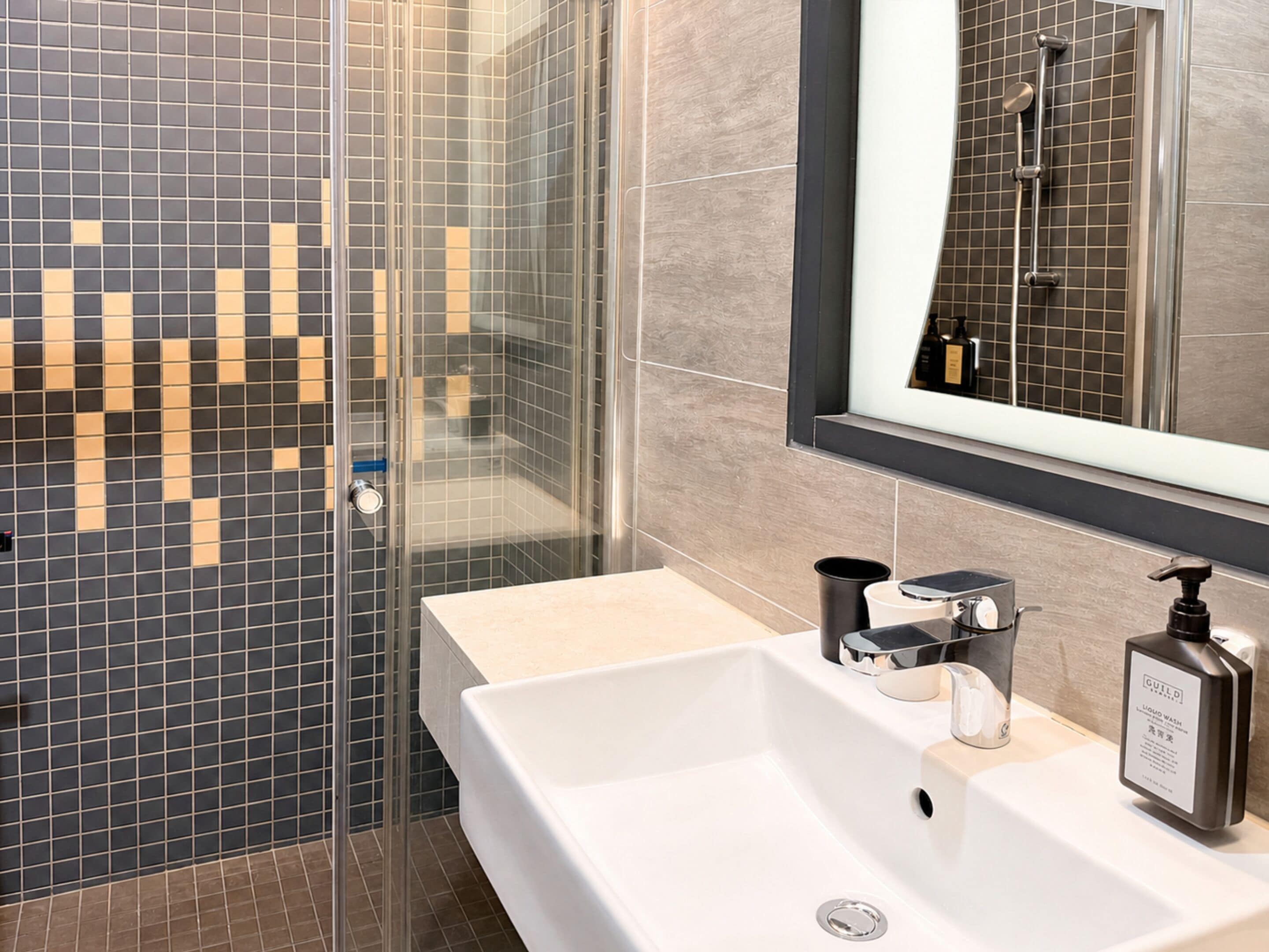 A modern bathroom with a glass shower enclosure, a white sink with chrome fixtures, and a mirror with a black frame.