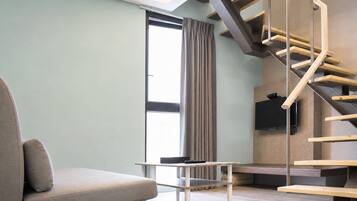 Uma sala de estar moderna com um sofá, uma mesa, uma TV fixada na parede e uma escada de madeira.