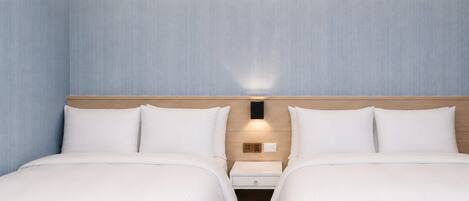 Hotellihuone, jossa on kaksi sänkyä, puinen pääty ja yöpöytä sekä seinään kiinnitetty valaisin.