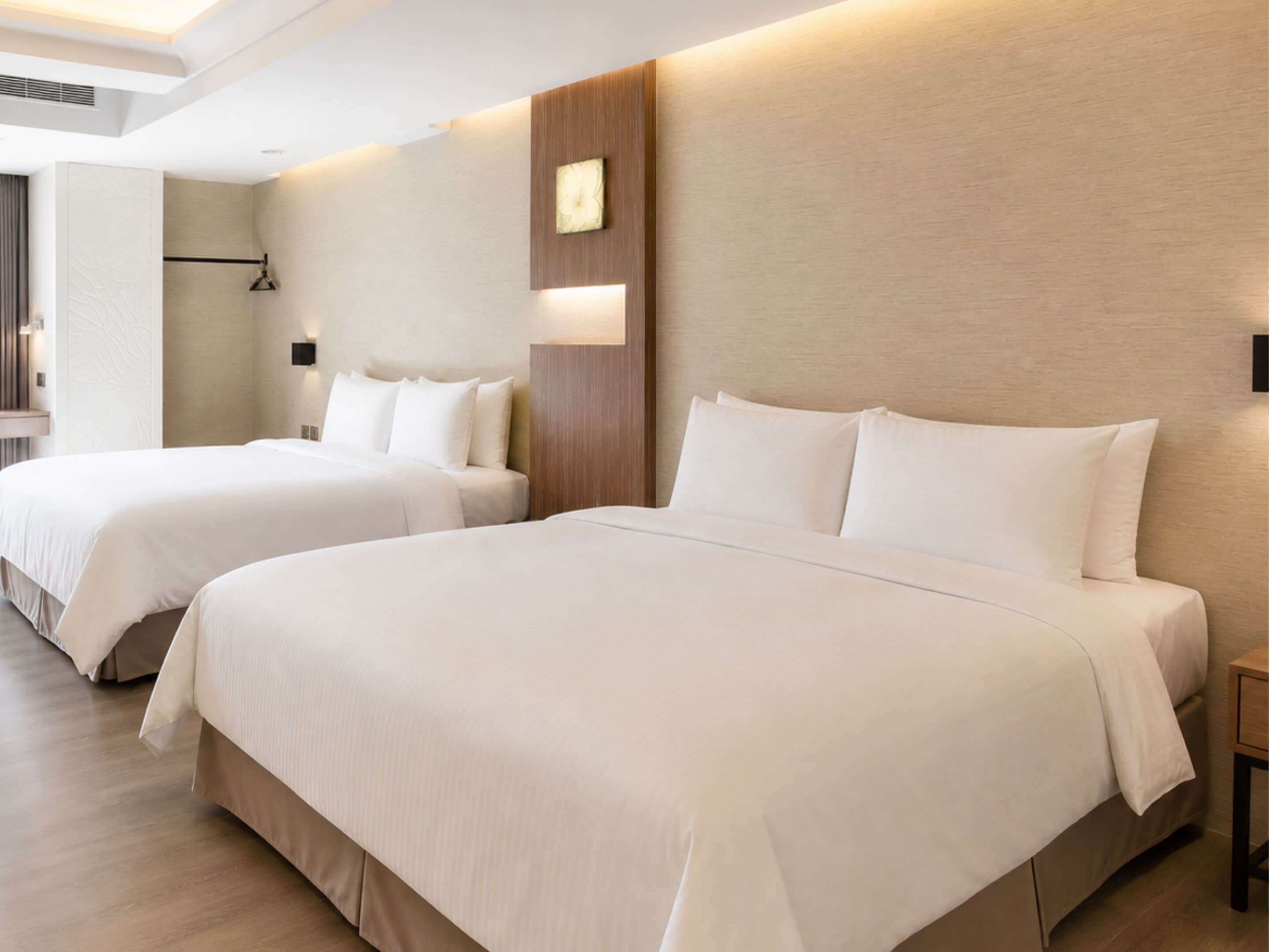 A hotel room with two beds, a wooden headboard, a wall clock, and a modern light fixture.