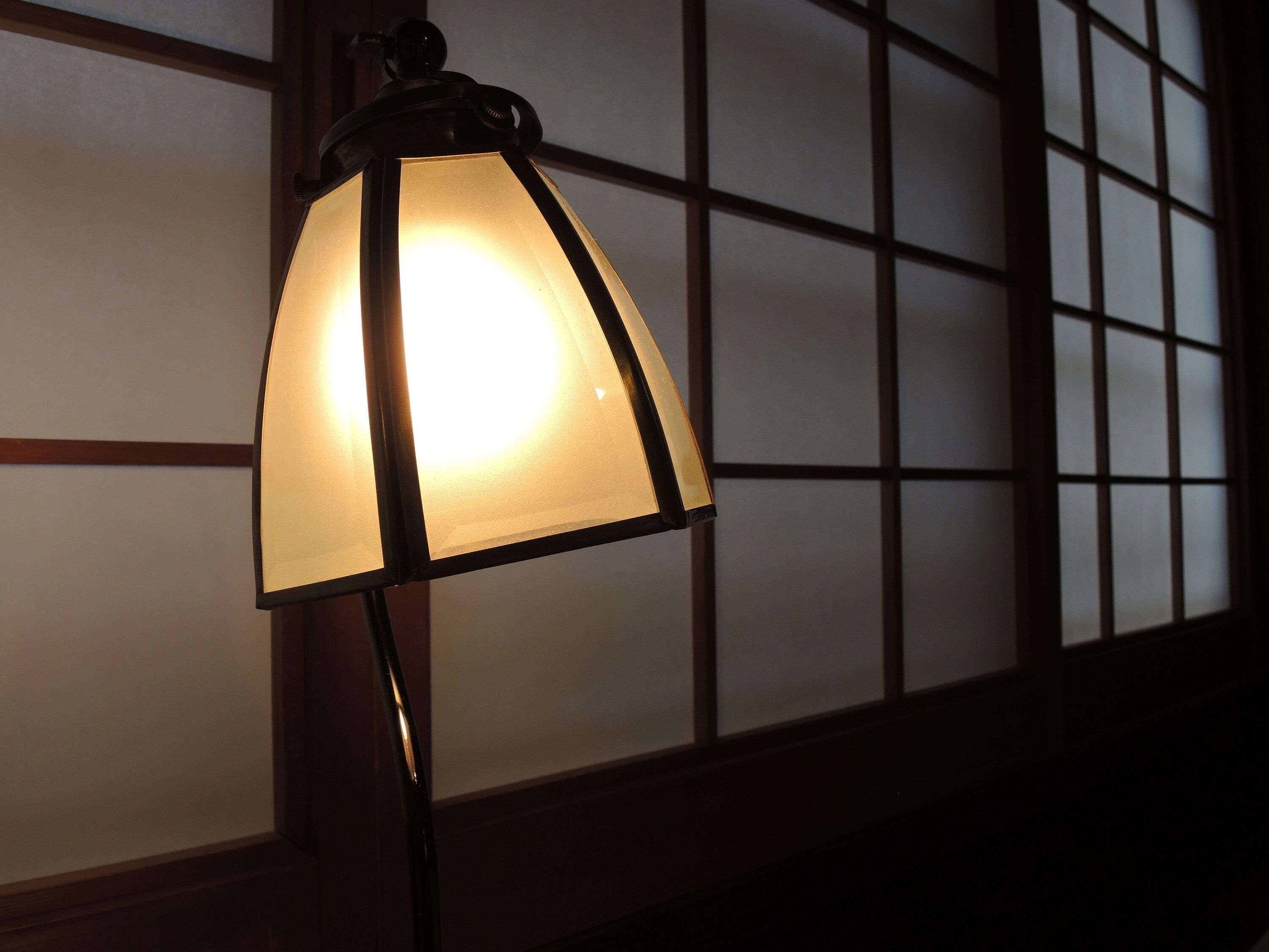 A lamp with a frosted glass shade, positioned in front of a window with a grid pattern.
