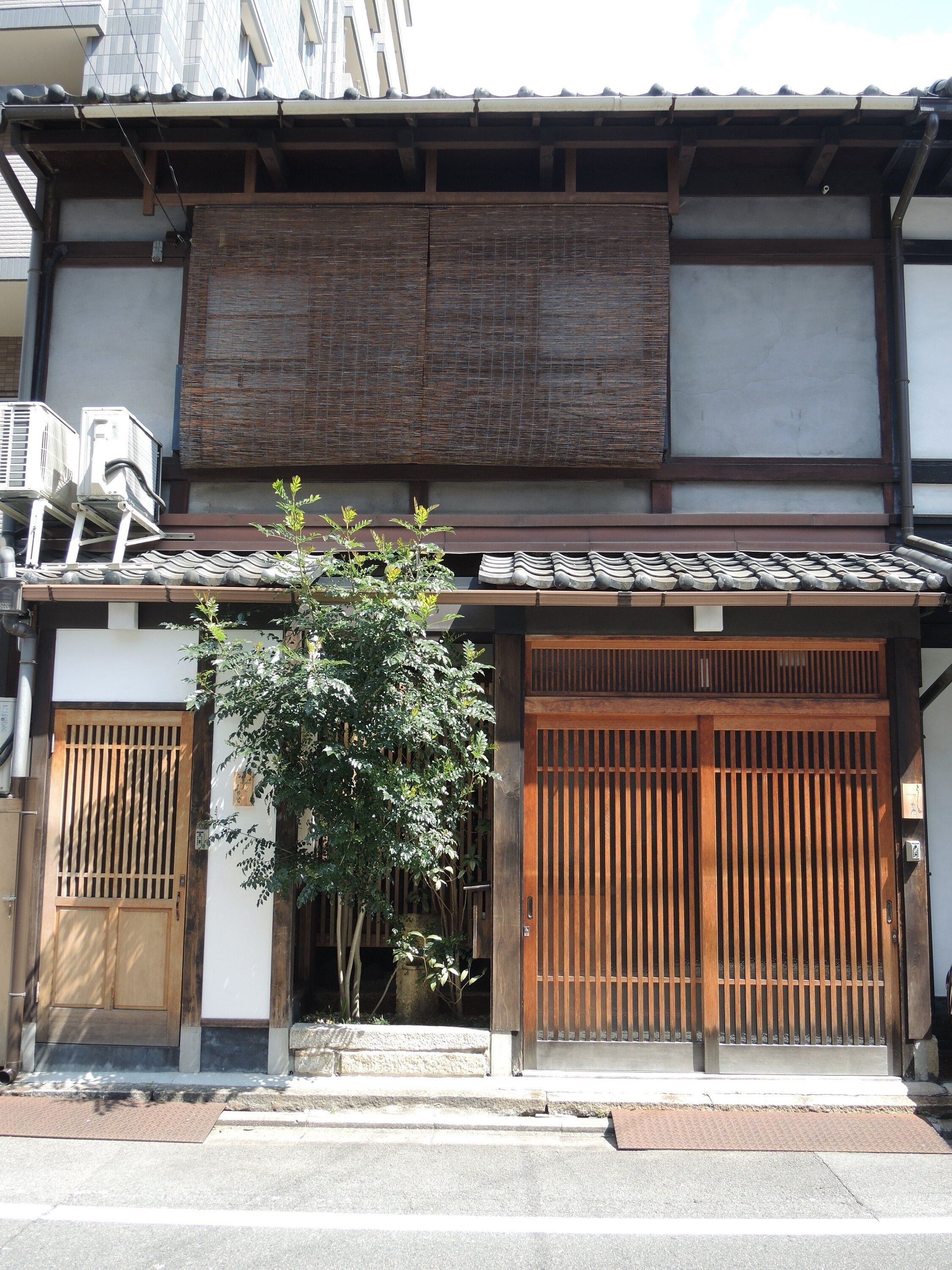 A traditional Japanese building with a tiled roof, wooden sliding doors, and a small tree in front.