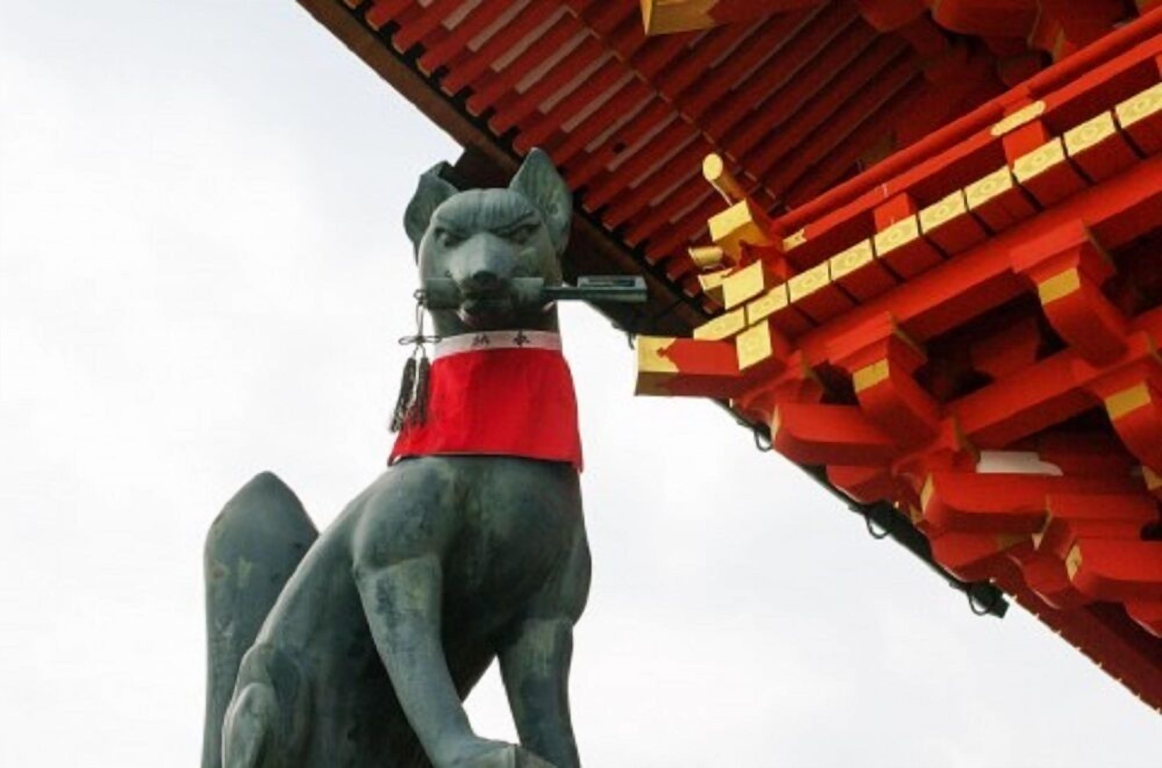 A statue of a dog wearing a red garment, positioned in front of a traditional red and gold building.