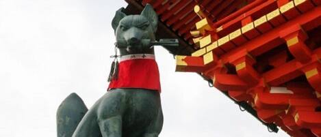 A statue of a dog wearing a red garment, positioned in front of a traditional red and gold building.