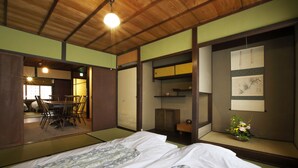 A traditional Japanese room with tatami flooring, a low wooden bed, a dining area with a table and chairs, and a sliding door leading to another room. - Kamiza-an Kamanza-tei (Kyoto)