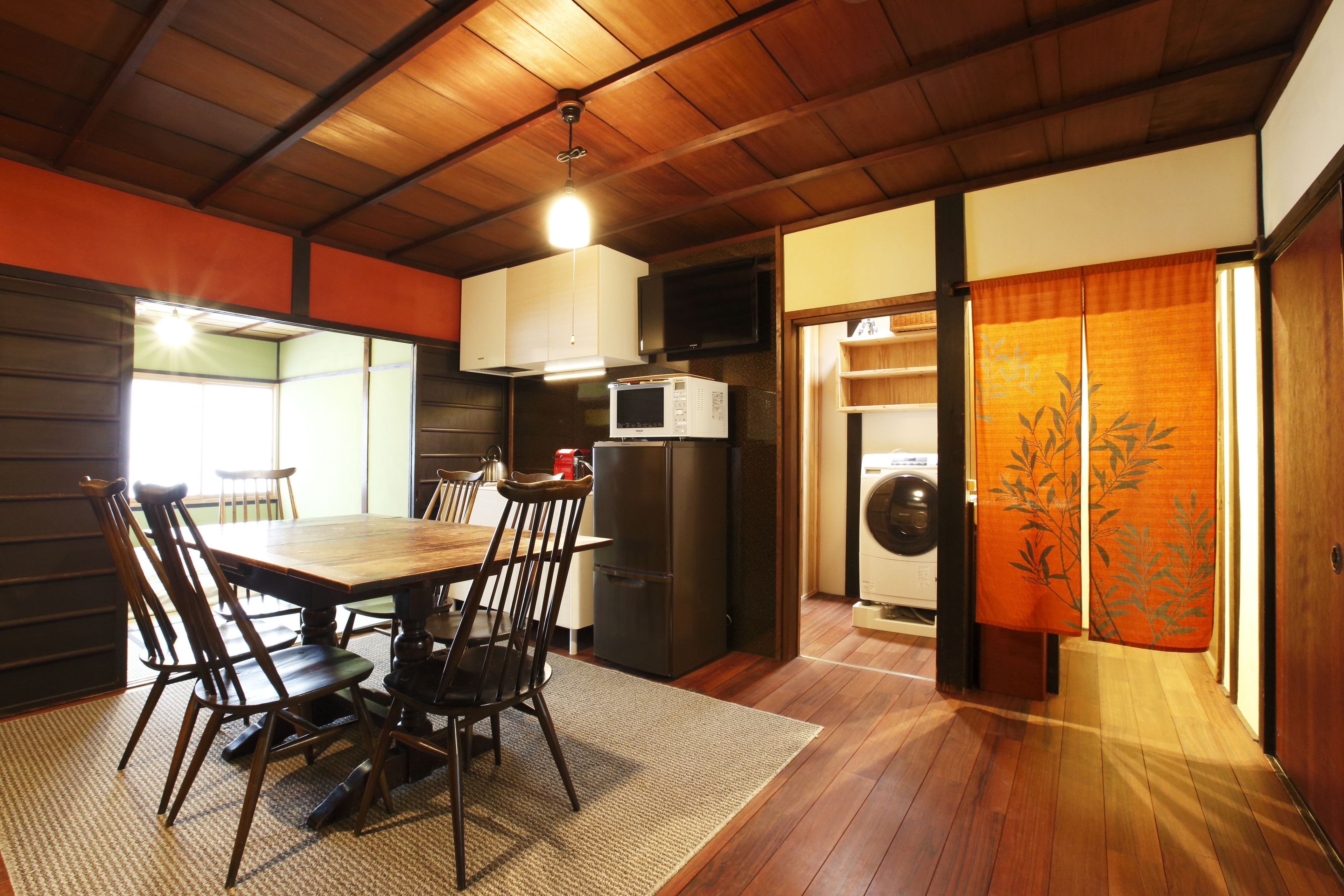 Une pièce de style japonais traditionnel, comprenant une table à manger en bois, des chaises, un réfrigérateur, un four à micro-ondes et un lave-linge.
