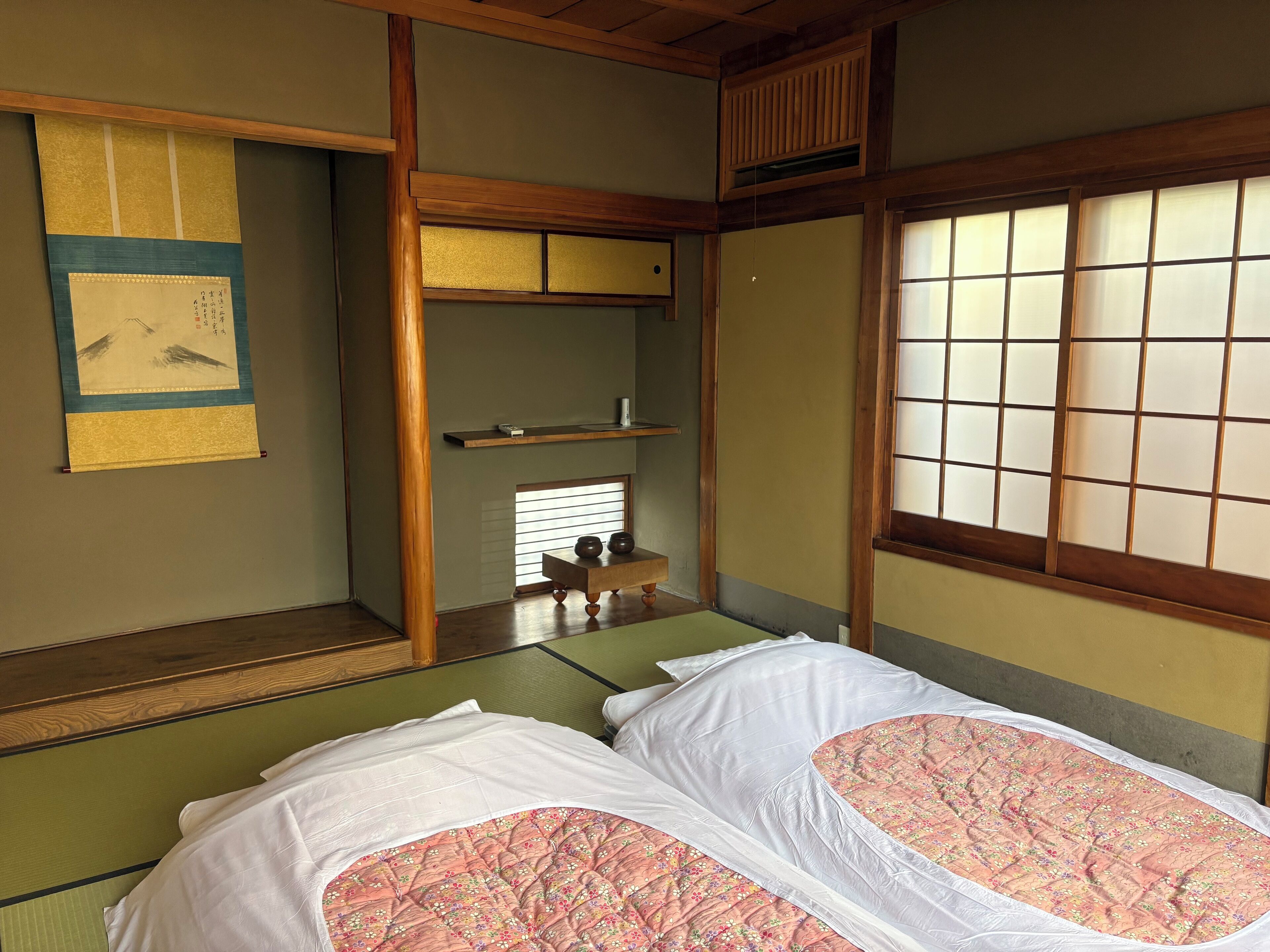A traditional Japanese room with tatami flooring, a futon bed, shoji screens, and a hanging scroll.