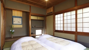 Een traditionele Japanse kamer met tatami vloerbedekking, een laag houten bed met wit beddengoed, een shoji-schuiframenraam en een hangende shoji-schuifdeur.