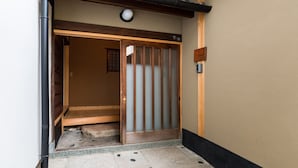 Een traditionele Japanse schuifdeur met houten frame en glaspanelen, die leidt naar een kamer met een tatami mat vloer en een klein raam.