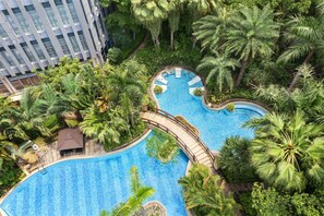 Una gran piscina de varios niveles rodeada de exuberante vegetación y palmeras, con un edificio moderno al fondo.
