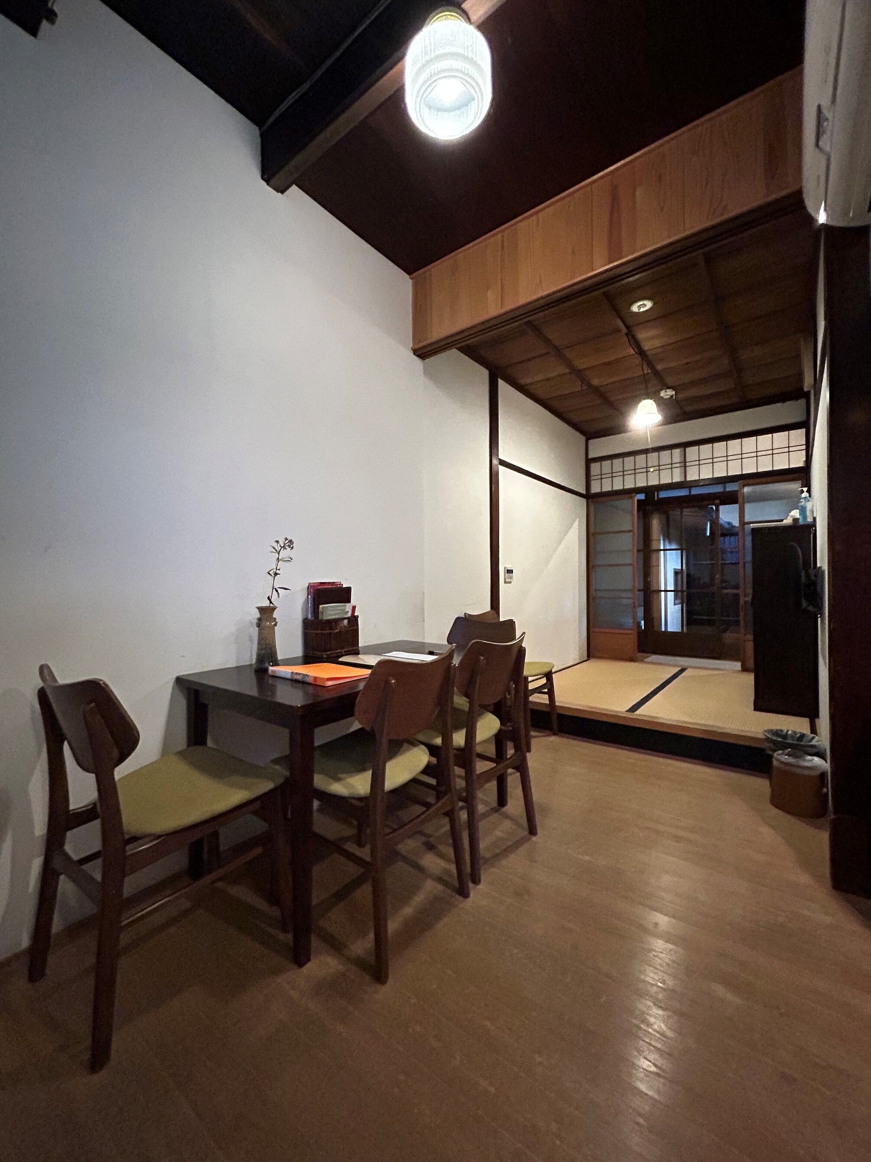 A dining area with a wooden table and chairs, a vase with flowers, and a view of a traditional Japanese room.