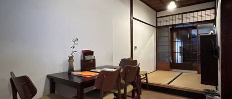 A dining area with a wooden table and chairs, a vase with flowers, and a view of a traditional Japanese room.