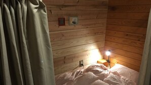 A cozy cabin room with a bed, a nightstand with a lamp, and wooden walls. - Guest House Coco Garage - Hostel (Kirishima)
