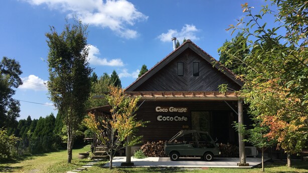 A rustic wooden building with a sign reading "Coco Garage Coco Cafe" and a parked vehicle in front. - Guest House Coco Garage - Hostel (Kirishima)