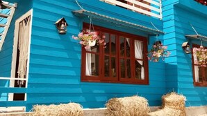 Een blauw gebouw met een wit balkon, rode raamkozijnen en bloembakken met bloemen.