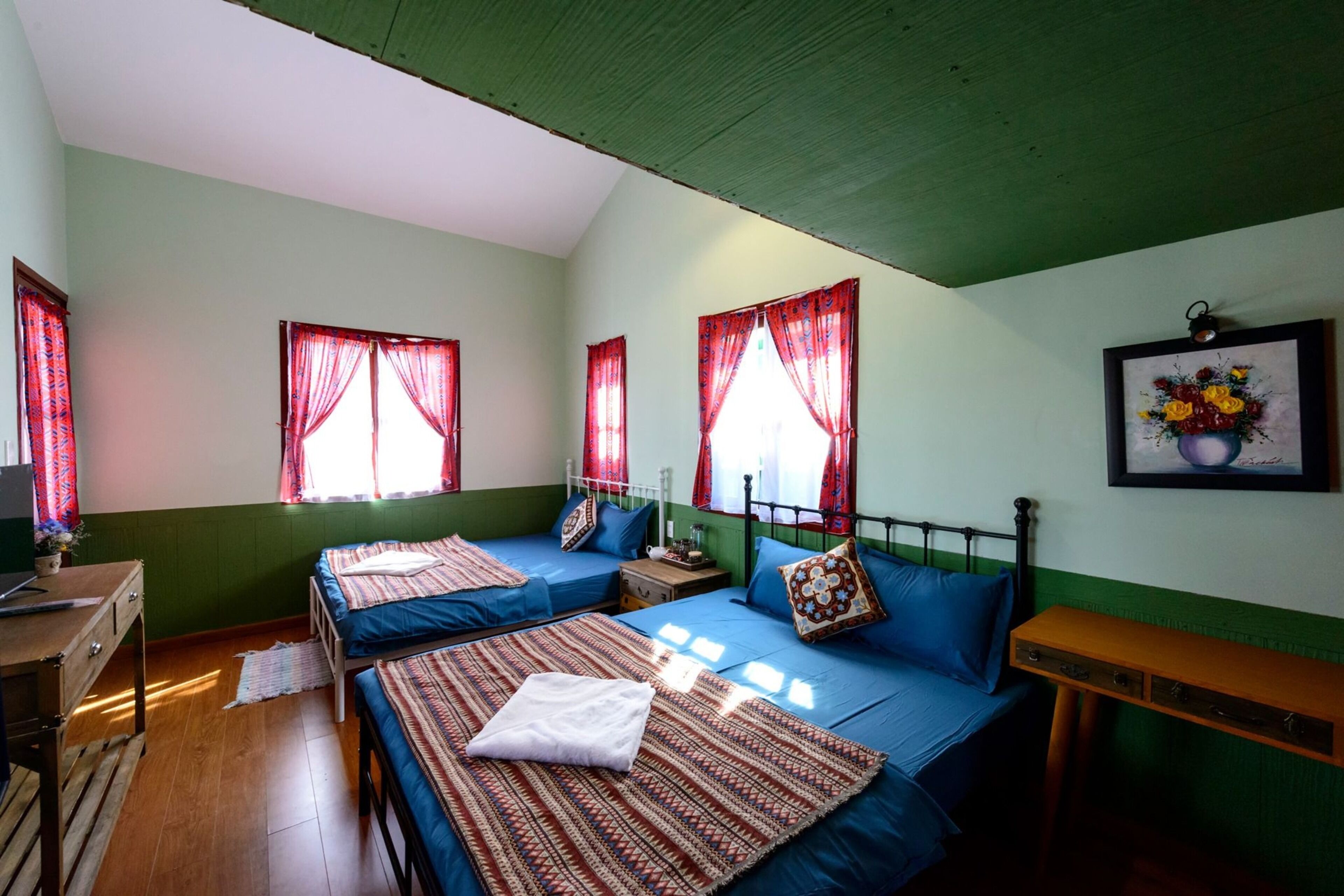 A room with two beds, a wooden dresser, a small table, and a wall-mounted picture.
