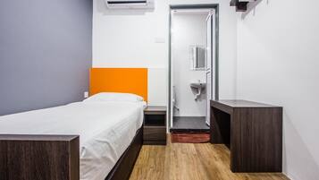 A compact hotel room with a single bed, a small bathroom, and a wooden floor.
