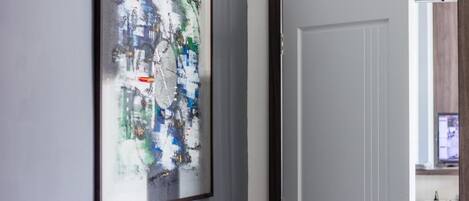Un pasillo con un cuadro abstracto enmarcado en la pared y una puerta cerrada.