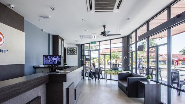 Um hall moderno de hotel com uma receção, uma televisão e uma área de estar com amplas janelas.