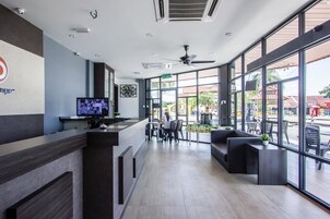 Un moderno vestíbulo de hotel con una recepción, un televisor y una zona de estar con ventanas amplias.