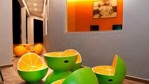 Um interior moderno com cadeiras únicas em laranja e verde, piso ladrilhado e uma obra de arte emoldurada na parede.