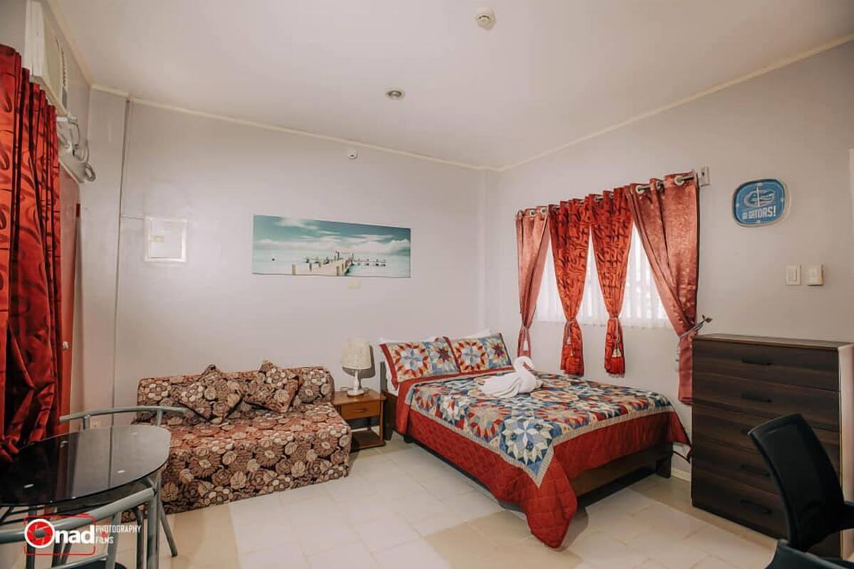 A bedroom with a bed, a desk, a chair, a sofa, and a painting on the wall.