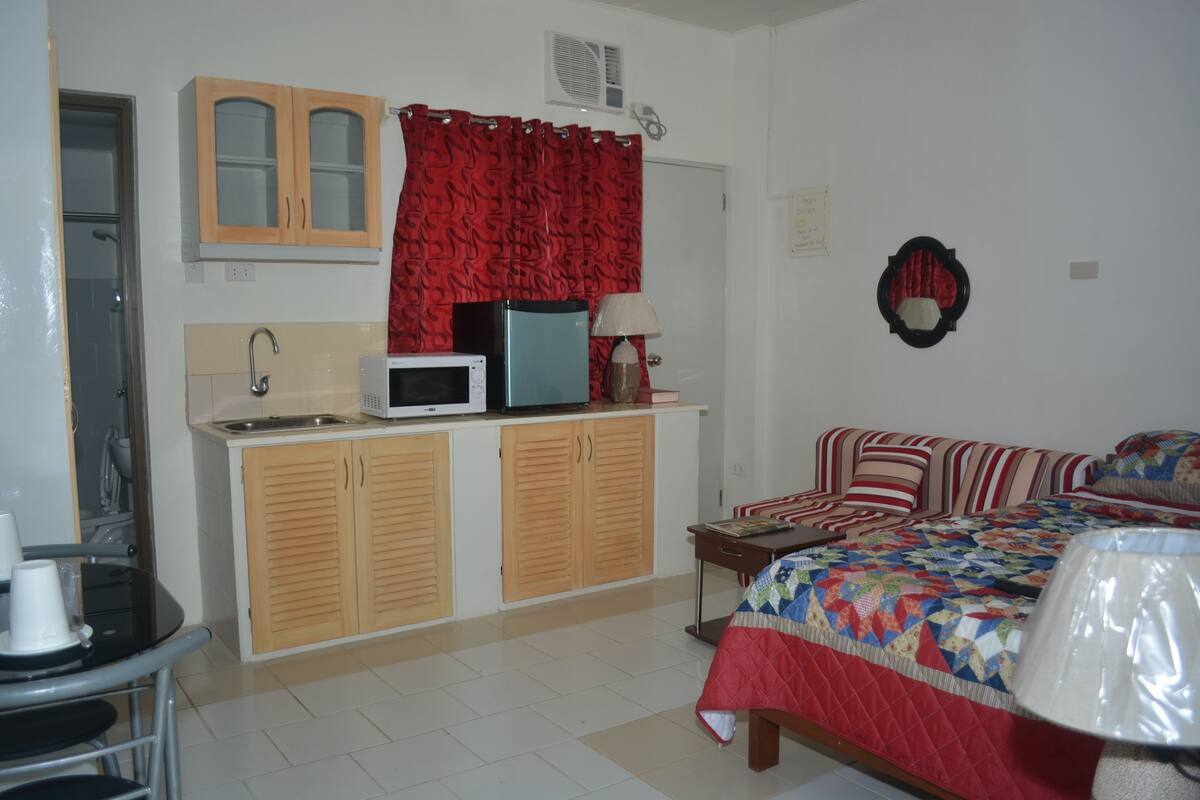 A room with a bed, a desk, a microwave, a sink, and a cabinet.