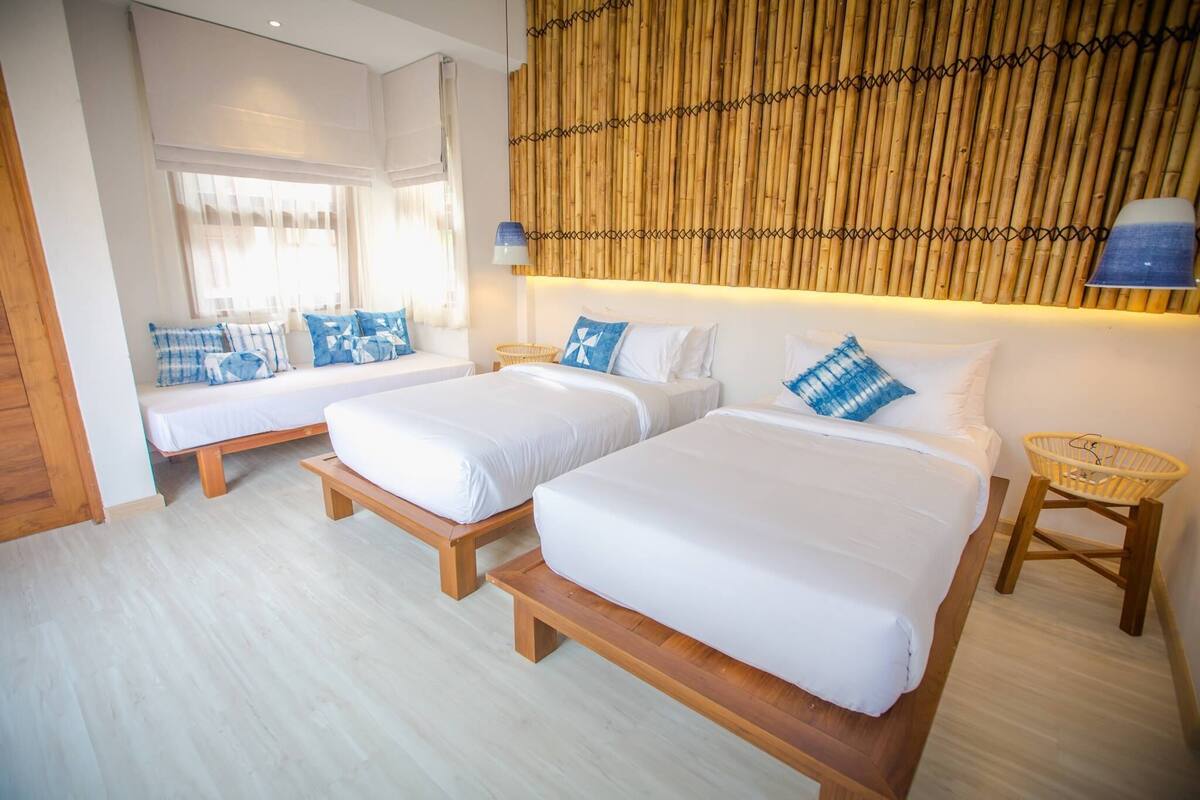A hotel room with two beds, a bamboo wall, and a window with curtains.