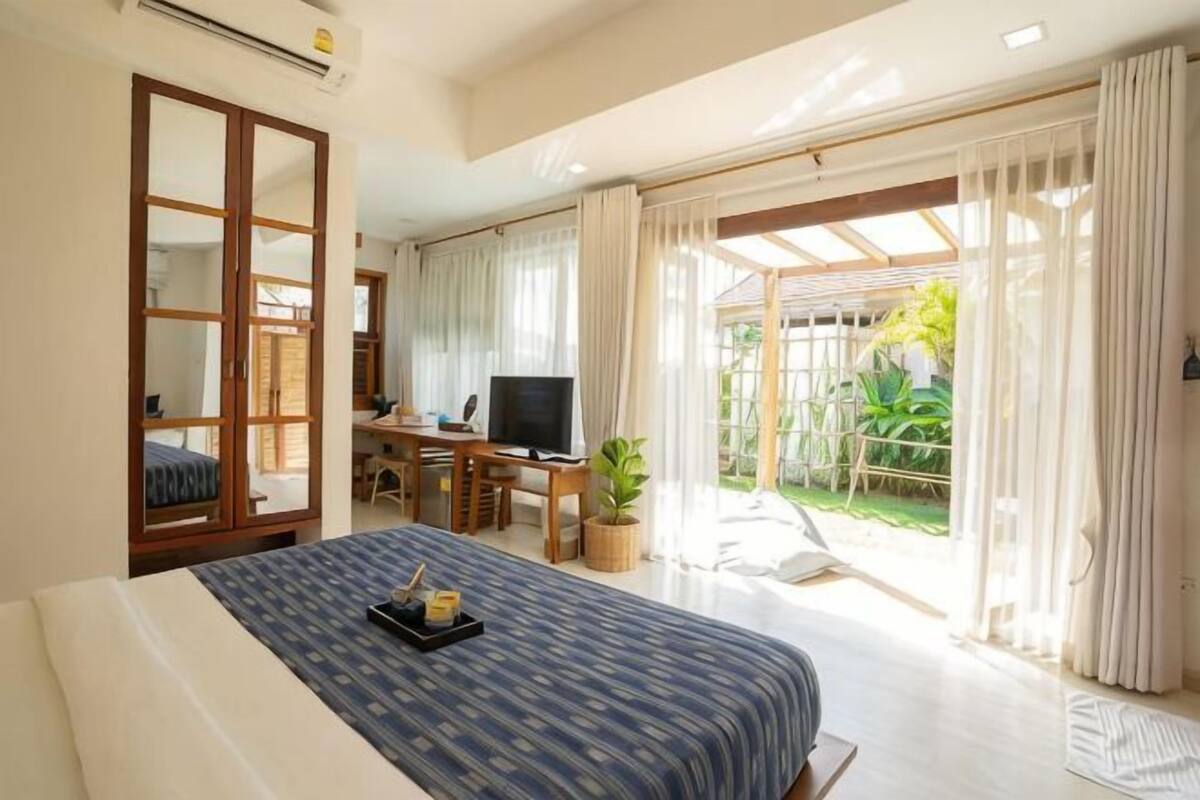 A bedroom with a bed, a desk with a TV, and a view of a garden.