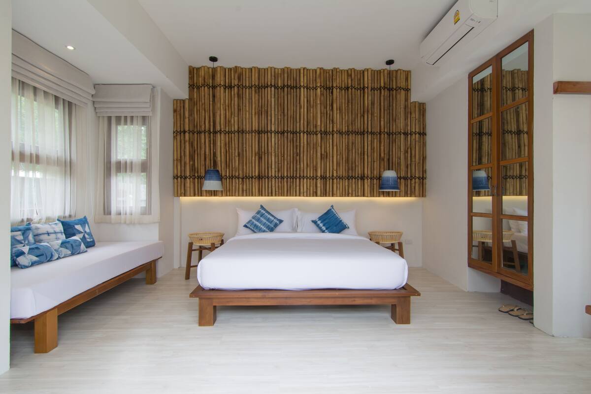 A bedroom with a large bed, a sofa, and a bamboo wall.