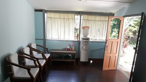 A room with a wooden chair, a small table with a tissue box, a water dispenser, and a door leading outside. - Kyaw Ngapali Lodge (Ngapali)