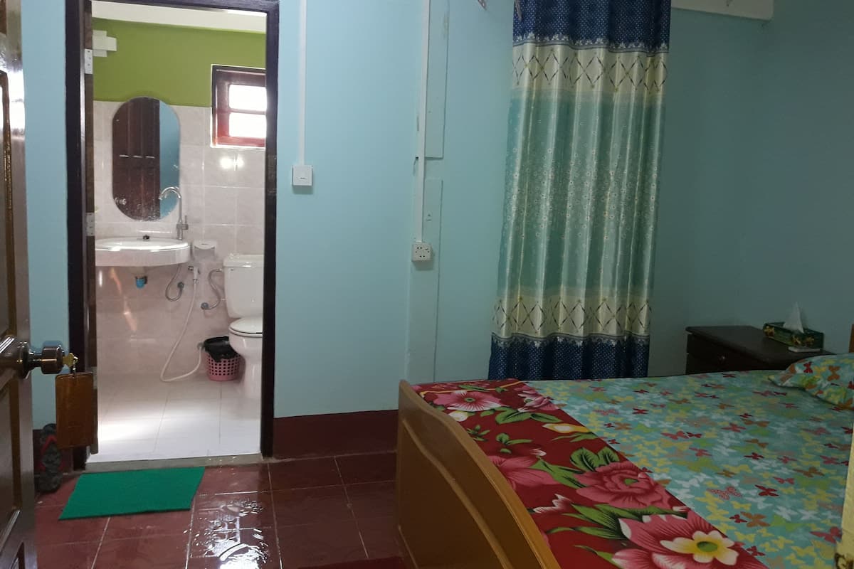 Une chambre à coucher avec un lit, un tapis vert, une salle de bain avec un lavabo et des toilettes, et un rideau.