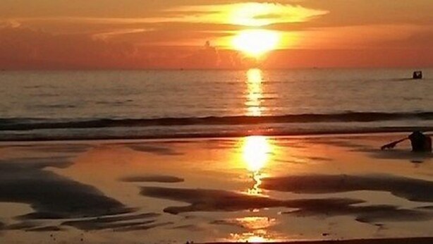 A sunset over a beach with calm waters and a person in the water. - Kyaw Ngapali Lodge (Ngapali)