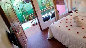 A hotel room with a bed, a wooden door, a window with a view of greenery, and a balcony. - Kyaw Ngapali Lodge (Ngapali)