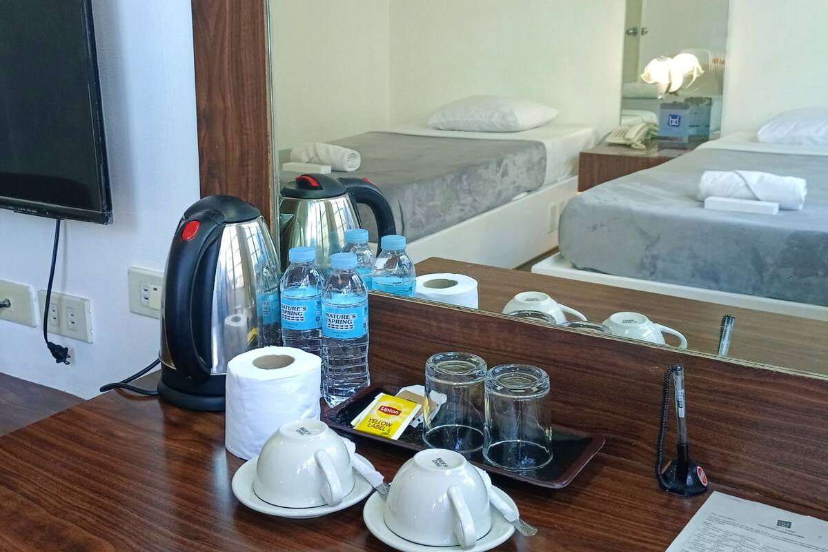 Une chambre d’hôtel équipée d’un bureau en bois, d’une bouilloire, de bouteilles d’eau, de thé et d’un téléphone.