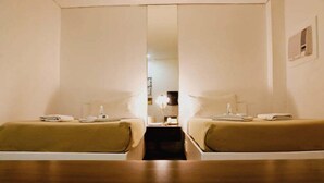 Habitación de hotel con dos camas, suelo de madera y una mesita de noche con lámpara entre ellas.