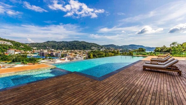 A wooden deck with a pool and lounge chairs overlooking a beach and a town.