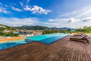 A wooden deck with a pool and lounge chairs overlooking a beach and a town. - Q Conzept Condominium (Karon)