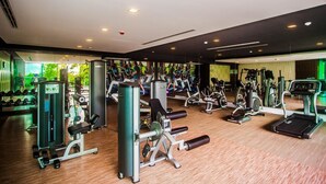 A gym with various exercise machines, mirrors, and a wooden floor.