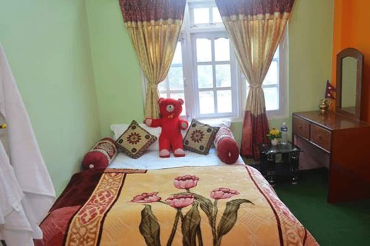 A bedroom with a bed, a red teddy bear, a dresser, and a window with curtains.