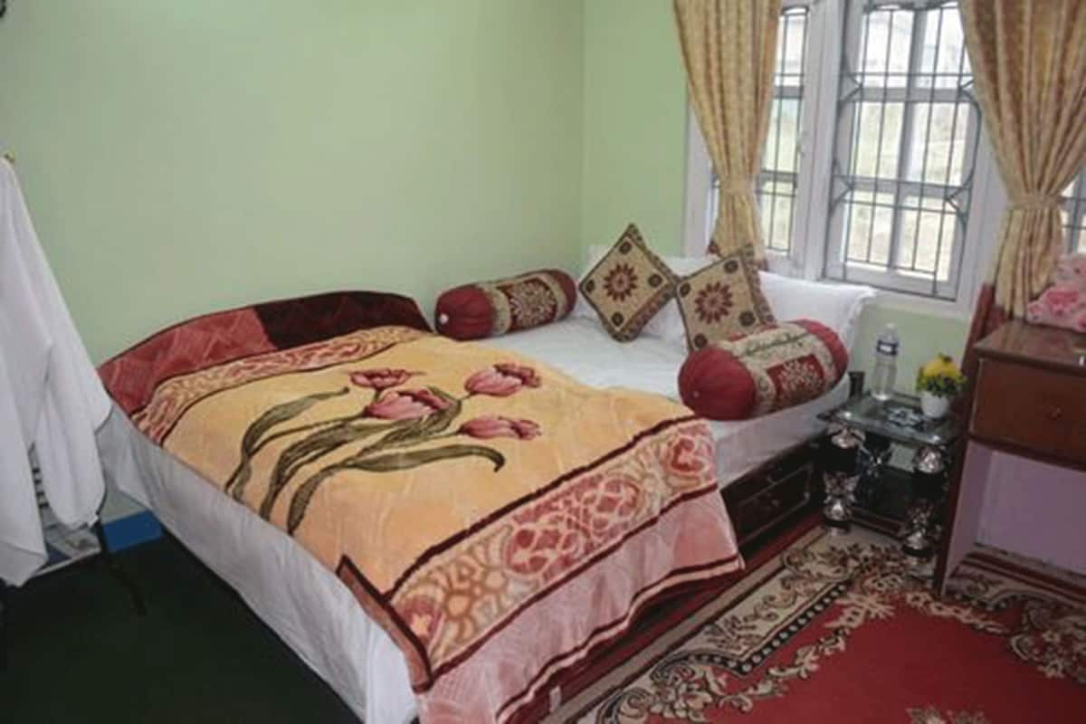 A bedroom with a bed, pillows, a nightstand, a dresser, and a window with curtains.