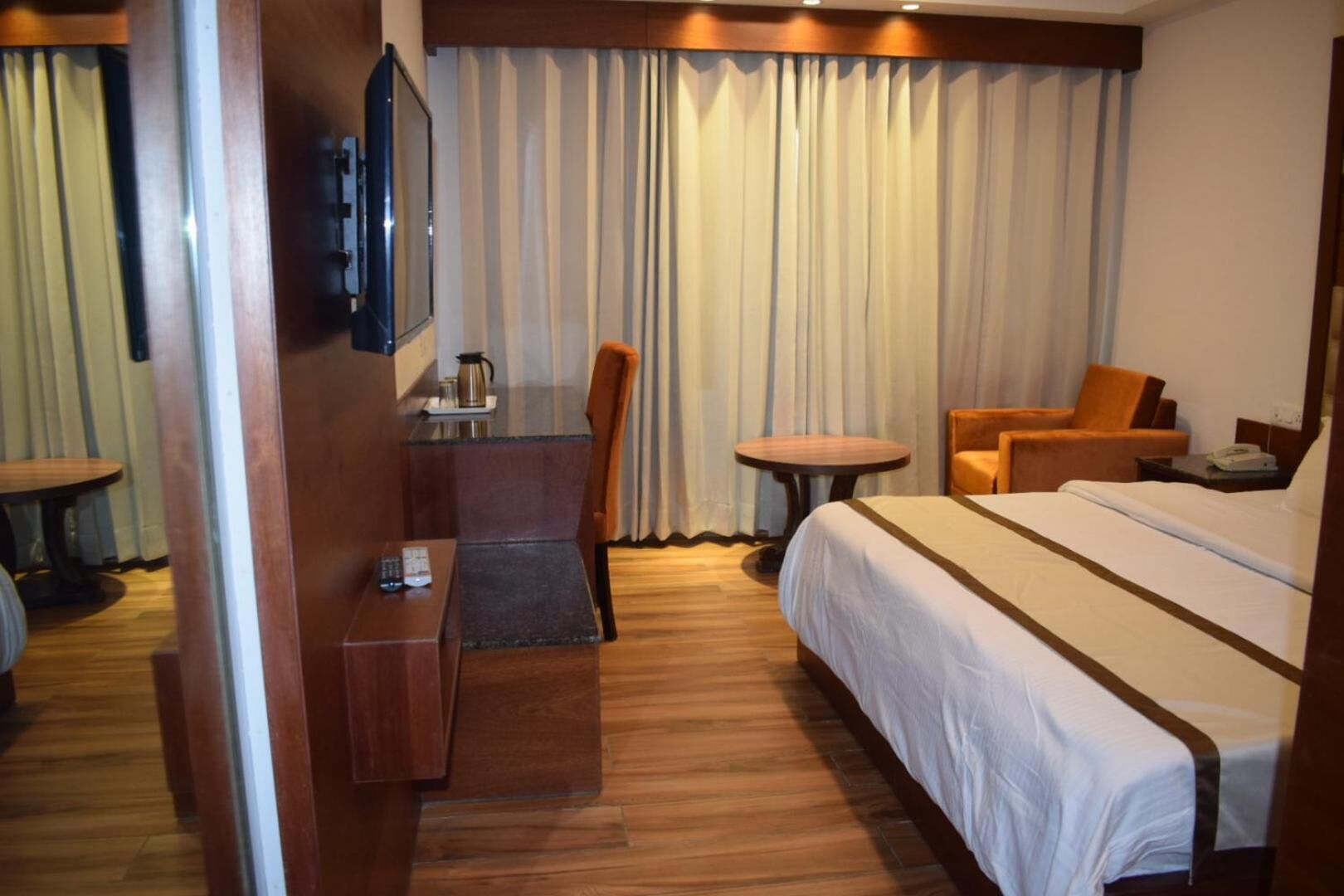 A hotel room with a bed, a desk, a chair, a small table, and a television.