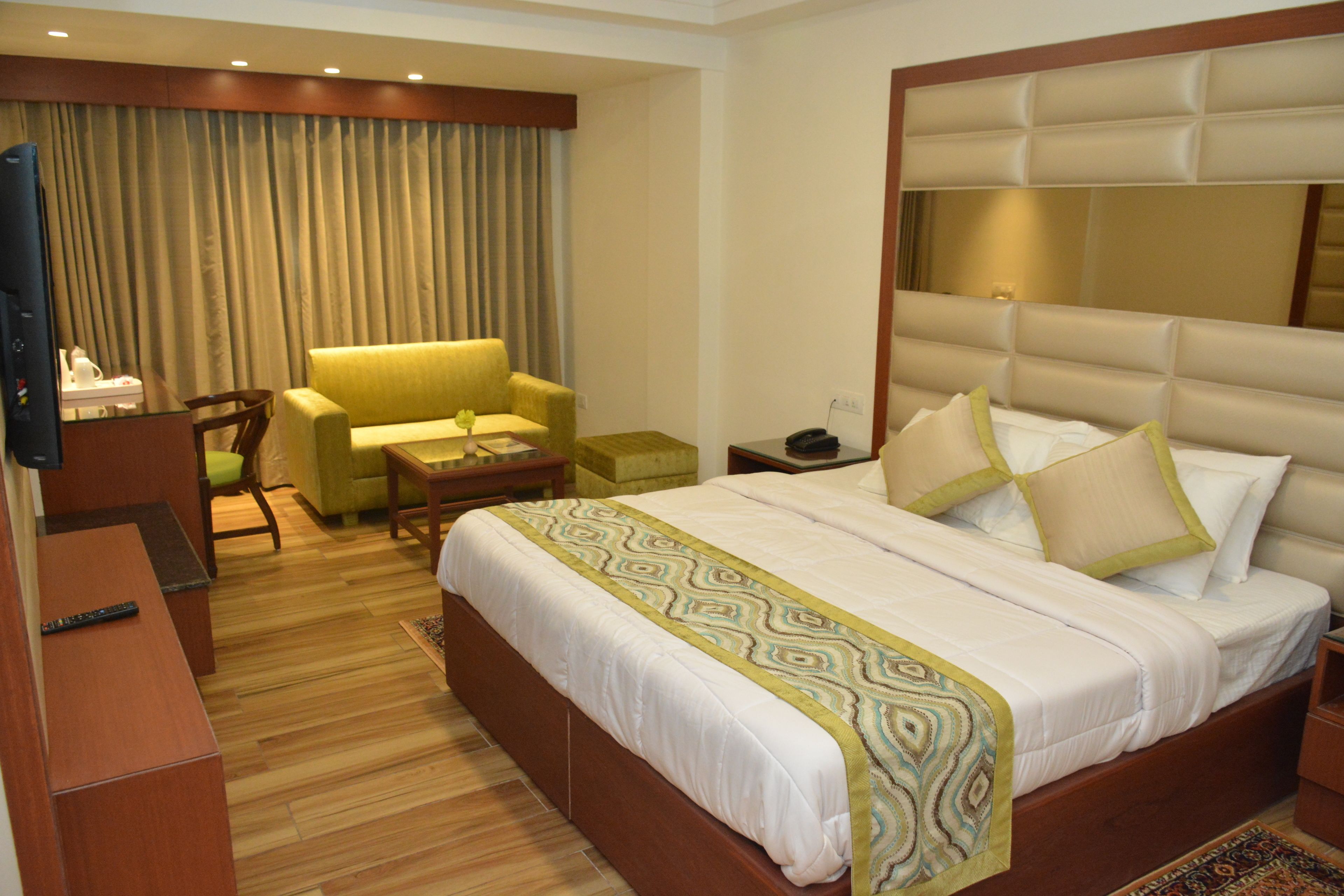 Habitación de hotel con una cama grande, un sofá, un escritorio con televisor y un espejo.