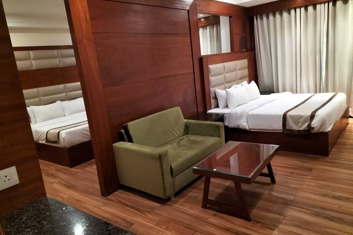 A hotel room with a bed, a sofa, a small table, and a mirror.